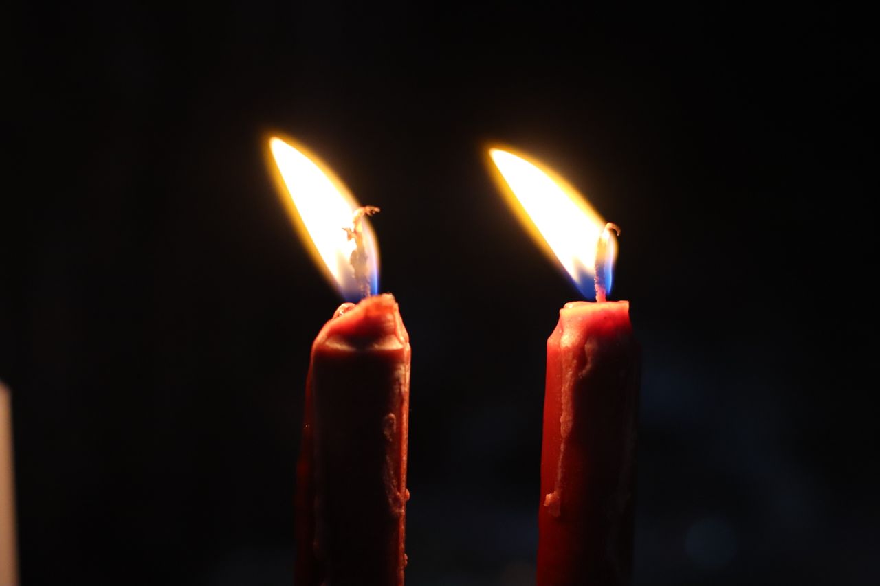 Warm glow of two lit candles casting light in darkness, symbolizing peace and spirituality.